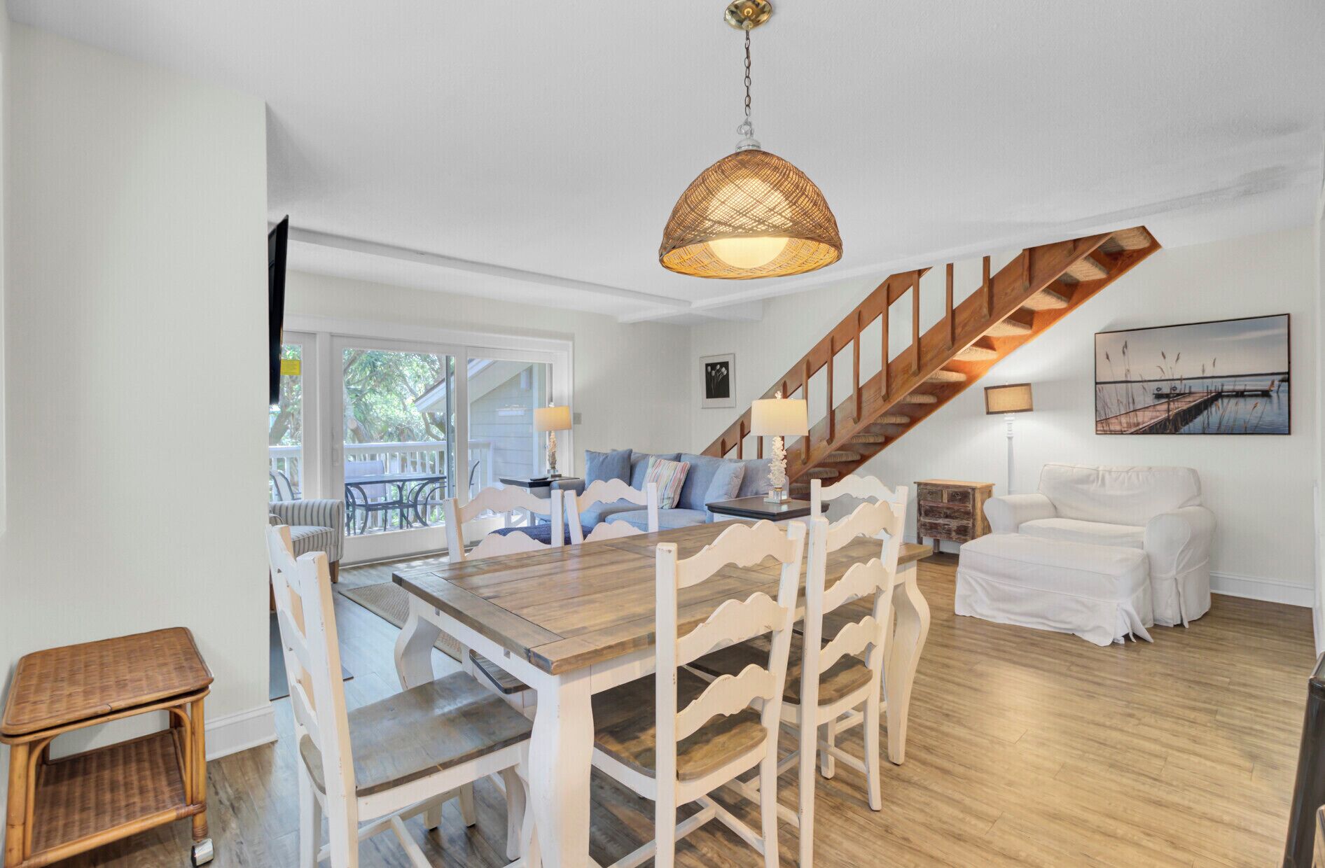A spacious dining area with a wooden table and white chairs, a staircase, and a view of the outdoors.