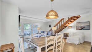 Un comedor amplio con una mesa de madera y sillas blancas, una escalera y vistas al exterior.
