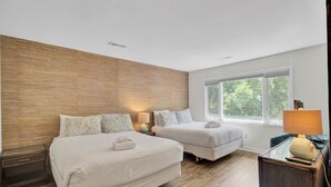 Una habitación de hotel con dos camas, una pared decorativa de madera, un ventanal con vistas a zonas verdes y un escritorio con lámpara.