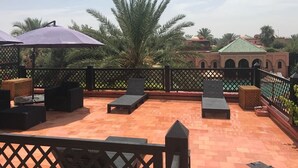 A rooftop terrace with lounge chairs, umbrellas, and a view of palm trees and a building with arches. - Villa with pool in Marrakech (Marrakech)