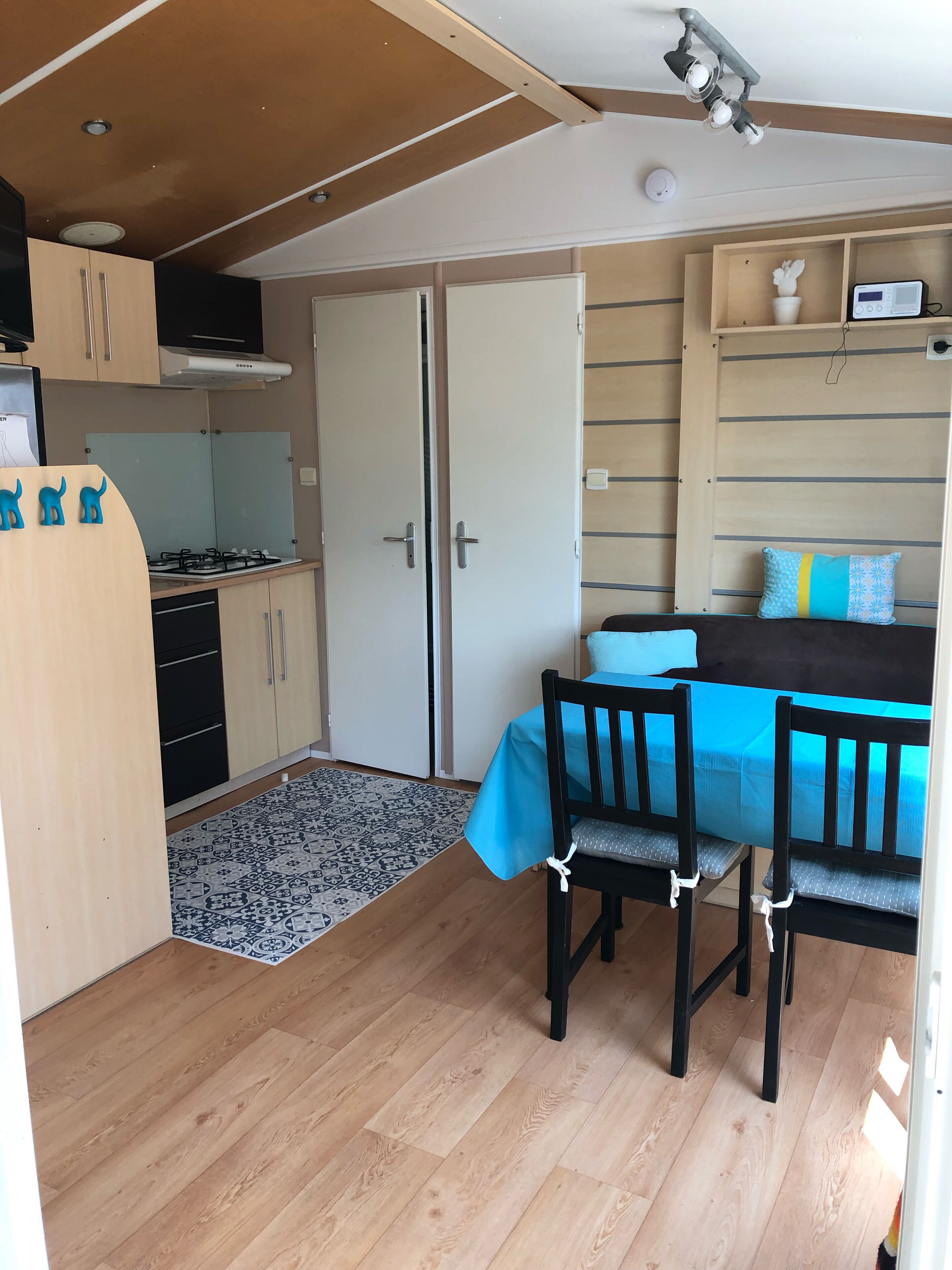 A compact living space with a kitchenette, a dining area with two chairs, a bed with a blue cover, and a small shelf with decorative items.