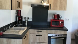 A compact kitchen with wooden cabinets, a black countertop, a coffee maker, a microwave, and a built-in oven. - Bed and Breakfast Sarlat Canada (Sarlat-la-Canéda)
