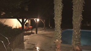 A nighttime outdoor area with a pool, palm trees, and a covered seating area with chairs. - Bed and Breakfast Sarlat Canada (Sarlat-la-Canéda)