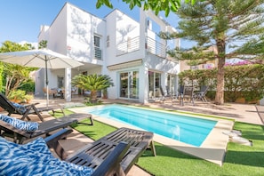 Une maison moderne dotée d’une piscine, de mobilier d’extérieur et d’un jardin bien entretenu.