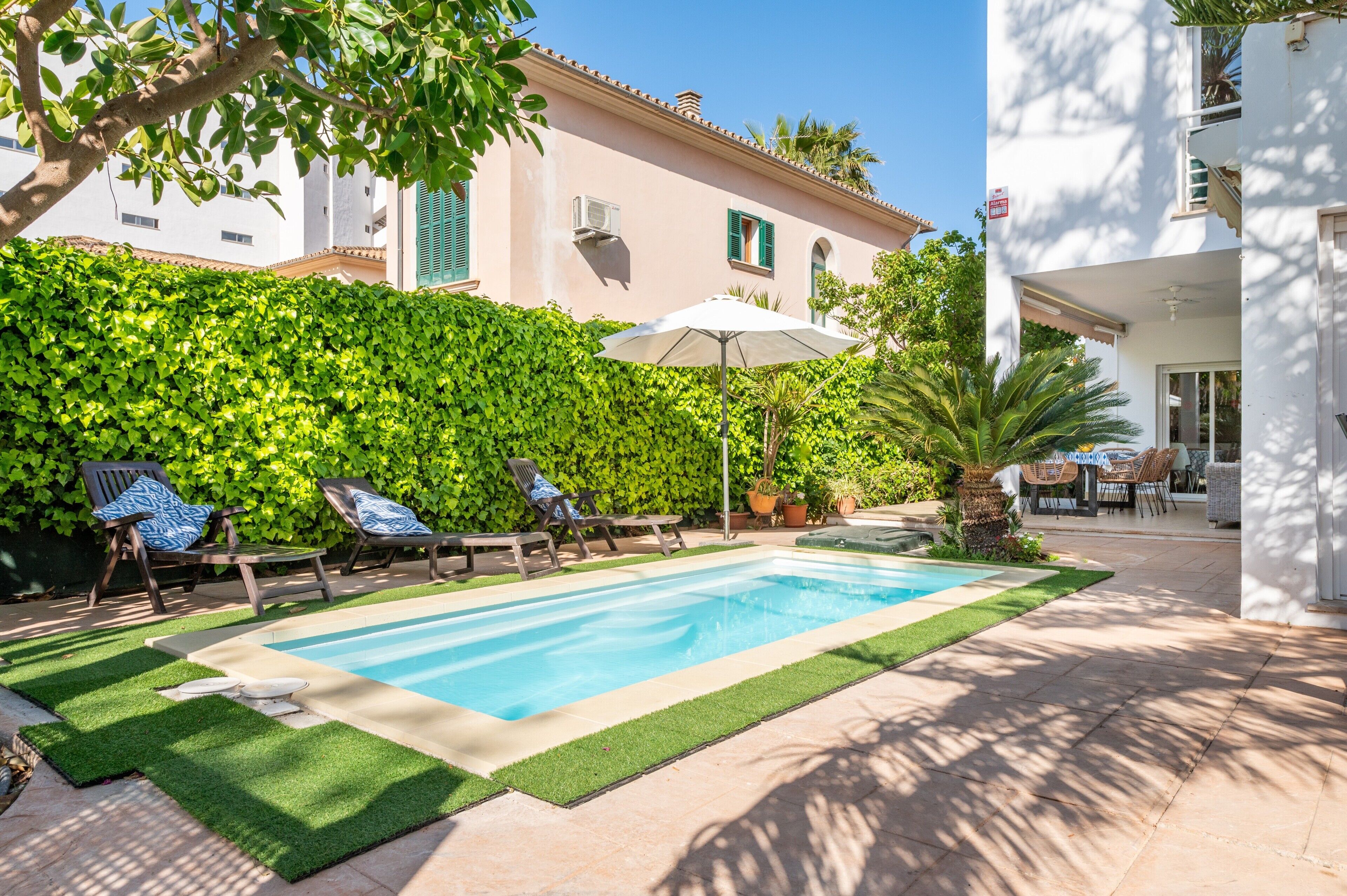 A swimming pool with lounge chairs, a patio area, and a building with a white facade and green shutters.