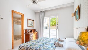 A bedroom with a bed, a wooden dresser, a ceiling fan, a door leading to a balcony, and a painting on the wall. - Holiday Home "Villa Mar - Can Bujosa" on the Beach (Palma de Mallorca)