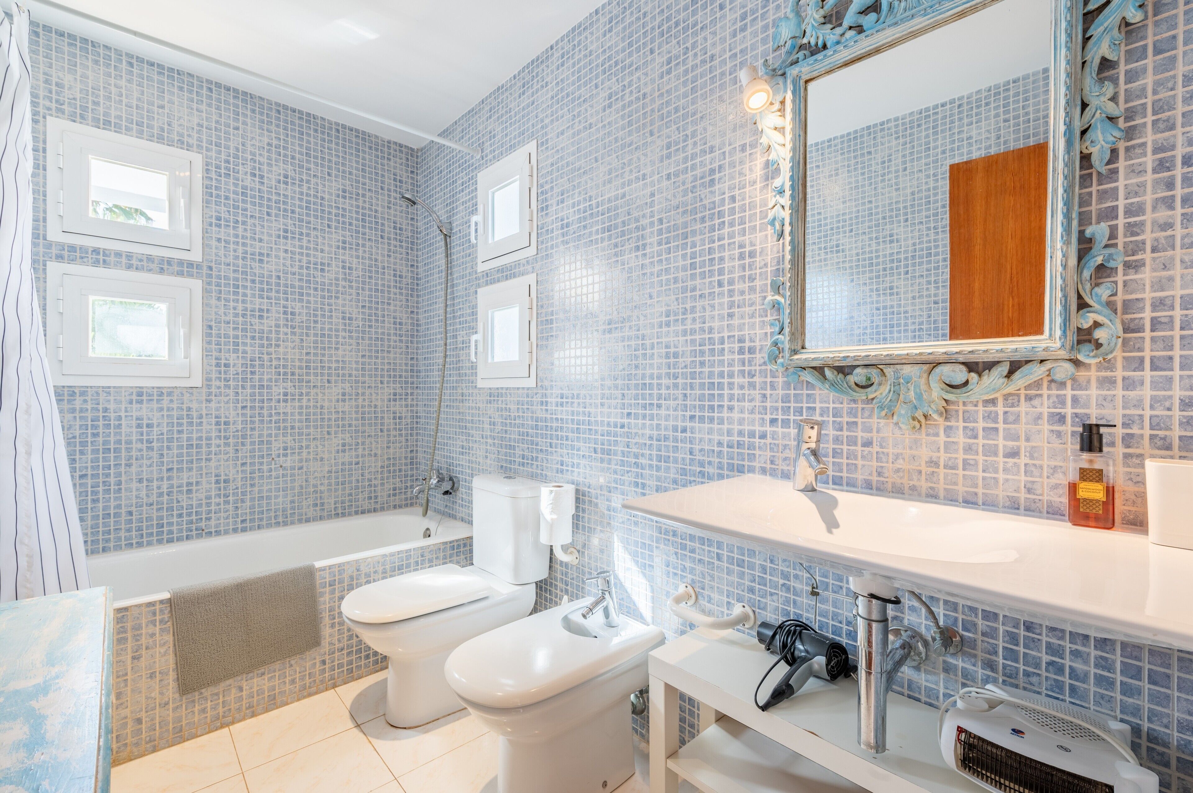 Une salle de bain avec une baignoire, deux toilettes, un lavabo et un miroir doté d’un cadre décoratif.