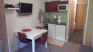 Eine kleine Küche mit einem weißen Tisch, roten Stühlen, einer Mikrowelle, einer Kaffeemaschine und einem Geschirrspüler.