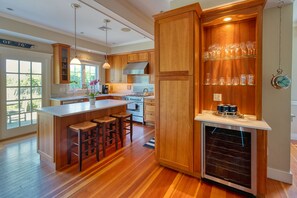 A modern kitchen with wooden cabinets, a central island with stools, a built-in oven, and a wine rack.