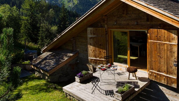 A wooden cabin with a sloped roof, a deck with outdoor furniture, and a mountain backdrop. - 5-Bedroom Chalet, Sauna, Norwegian Bath, Wifi, Sleeps 12 in La Clusaz (La Clusaz)