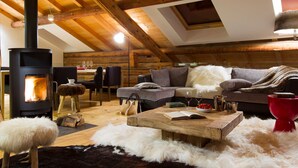 A cozy loft-style living room with a wooden ceiling, a fireplace, a sofa, a coffee table, and a dining area. - 5-Bedroom Chalet, Sauna, Norwegian Bath, Wifi, Sleeps 12 in La Clusaz (La Clusaz)