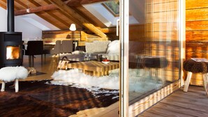 A cozy cabin interior with a wood-burning stove, a sofa, a dining table, and a glass door leading outside. - 5-Bedroom Chalet, Sauna, Norwegian Bath, Wifi, Sleeps 12 in La Clusaz (La Clusaz)