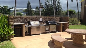 An outdoor grill area with a stone wall, a table, and a bench. - Maui Vista -  Fully Renovated, New Kitchen and Bathroom.  Best Location. (Kihei)