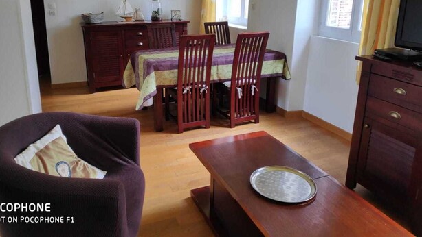 Zona pranzo con tavolo e sedie in legno, un divano, una televisione e una finestra con tende.