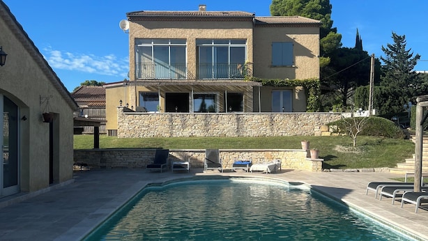 Una casa de dos pisos con piscina, muros de piedra y zona de estar al aire libre.