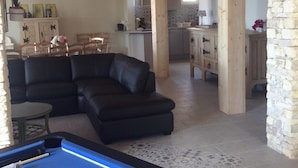 Una sala de estar acogedora con mesa de billar, sofá seccional y una cocina al fondo.