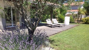 A garden with a wooden deck, two lounge chairs, and a large planter.