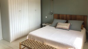 A bedroom with a bed, bedside table, lamp, and a woven bench.