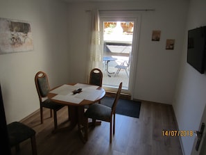 A small dining area with a table and four chairs, a door leading outside, and a wall-mounted TV.