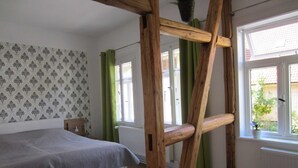Ein Schlafzimmer mit einem Bett, einer Holzleiter, einem Fenster mit Blick auf Grünflächen und strukturierter Wandpapier.