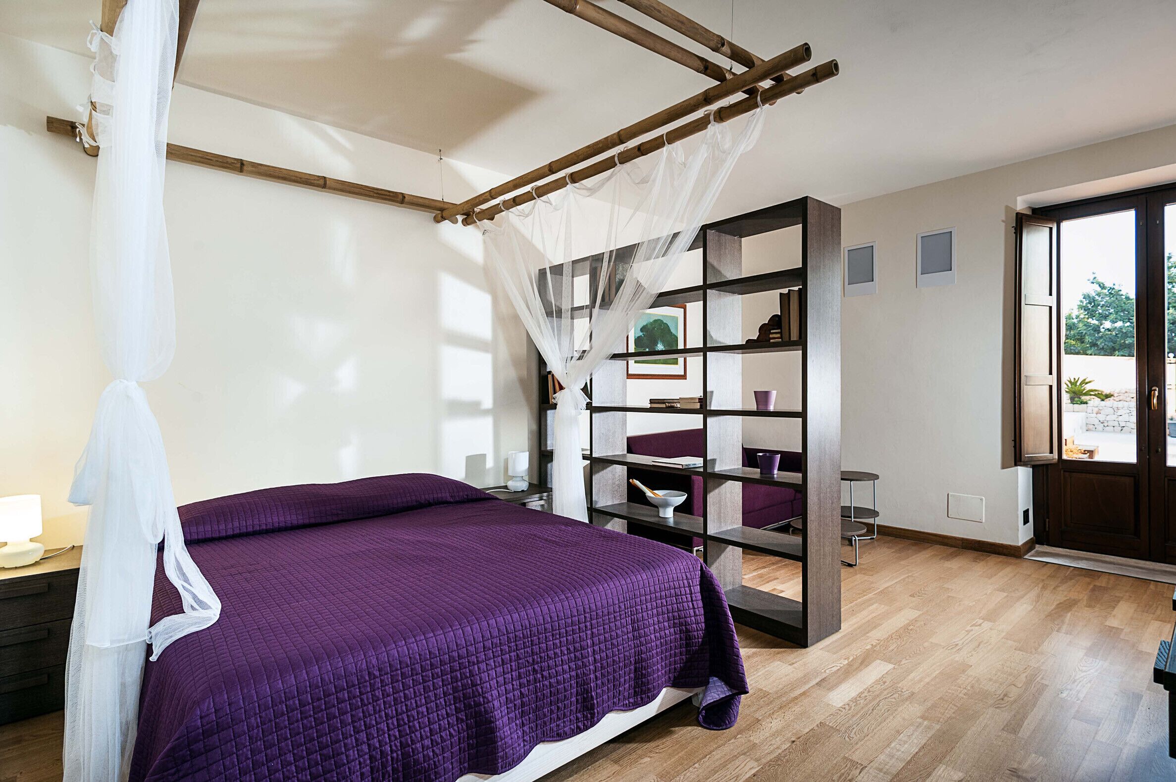 Quarto com uma cama grande, piso de madeira, estante de livros e janela com vista.
