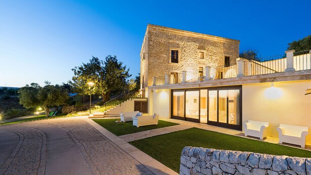 A modern building with a stone facade, large windows, and outdoor seating. - Villa with pool, wellness area and private tennis court (Scicli)