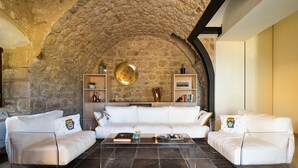 A living room with a stone ceiling, white leather sofas, a clear glass coffee table, and built-in shelves with decorative items. - Villa with pool, wellness area and private tennis court (Scicli)
