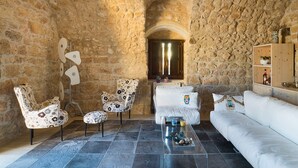 A stone-walled room with a white sofa, two patterned armchairs, a coffee table, and a wooden cabinet with decorative items. - Villa with pool, wellness area and private tennis court (Scicli)