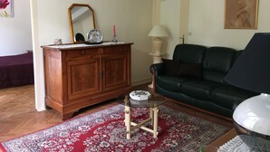 Ein Wohnzimmer mit einem Holzschrank, einem grünen Ledersofa, einem Glastisch und einem roten Teppich mit Muster.