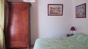 Ein Schlafzimmer mit einem Holzschrank, einem Bett mit grüner Decke und zwei gerahmten Bildern an der Wand.