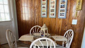 Un'area pranzo con parete rivestita in legno, un tavolo rotondo e quattro sedie bianche in vimini.
