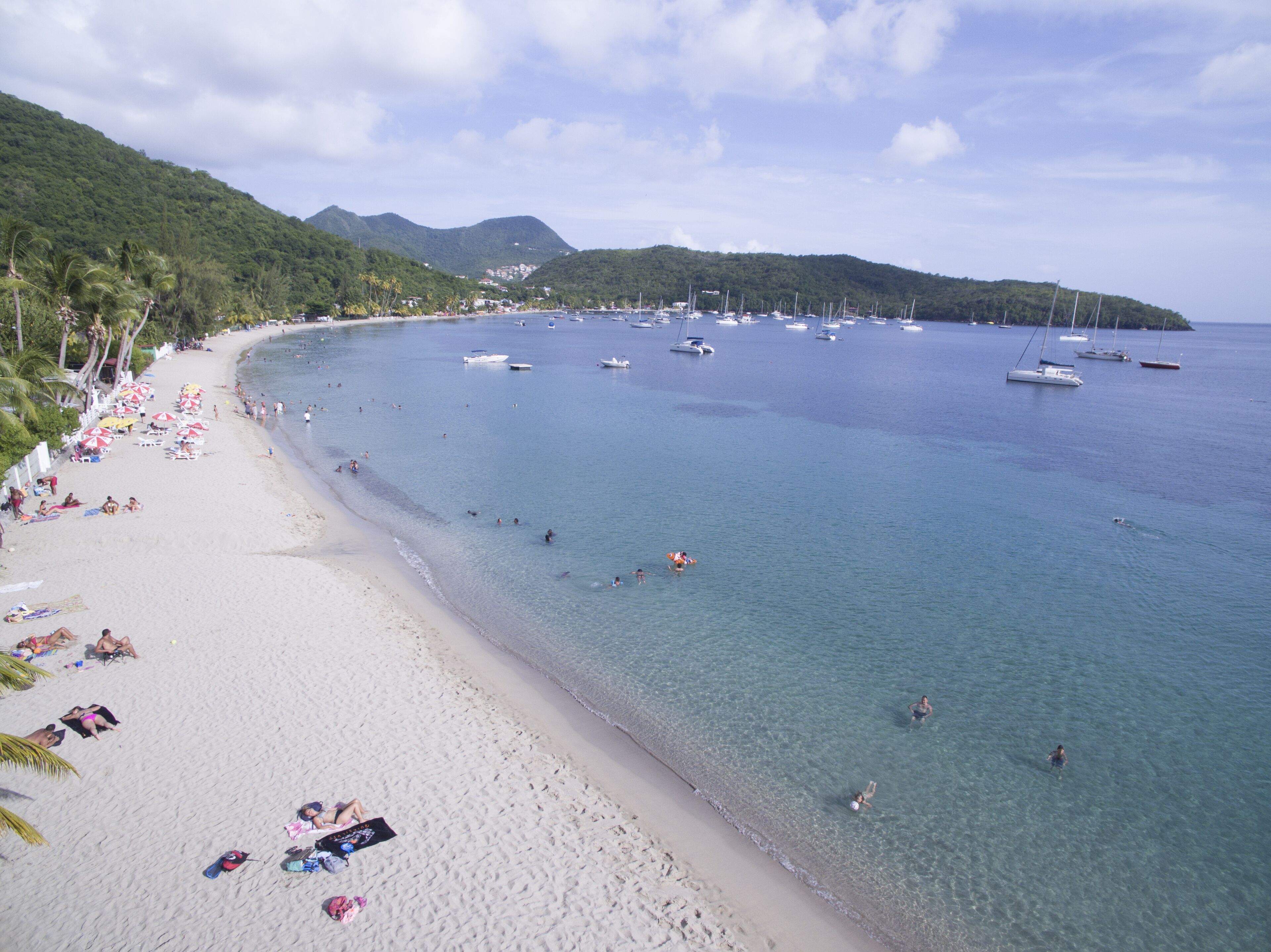 A beach with clear waters, a sandy shore, and boats in the distance.