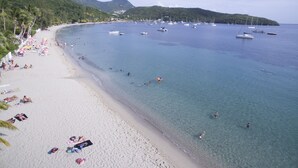 Une plage aux eaux cristallines, un rivage sablonneux et des bateaux à l’horizon.