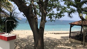 Une vue sur la plage avec un arbre, un kiosque et une balustrade blanche.