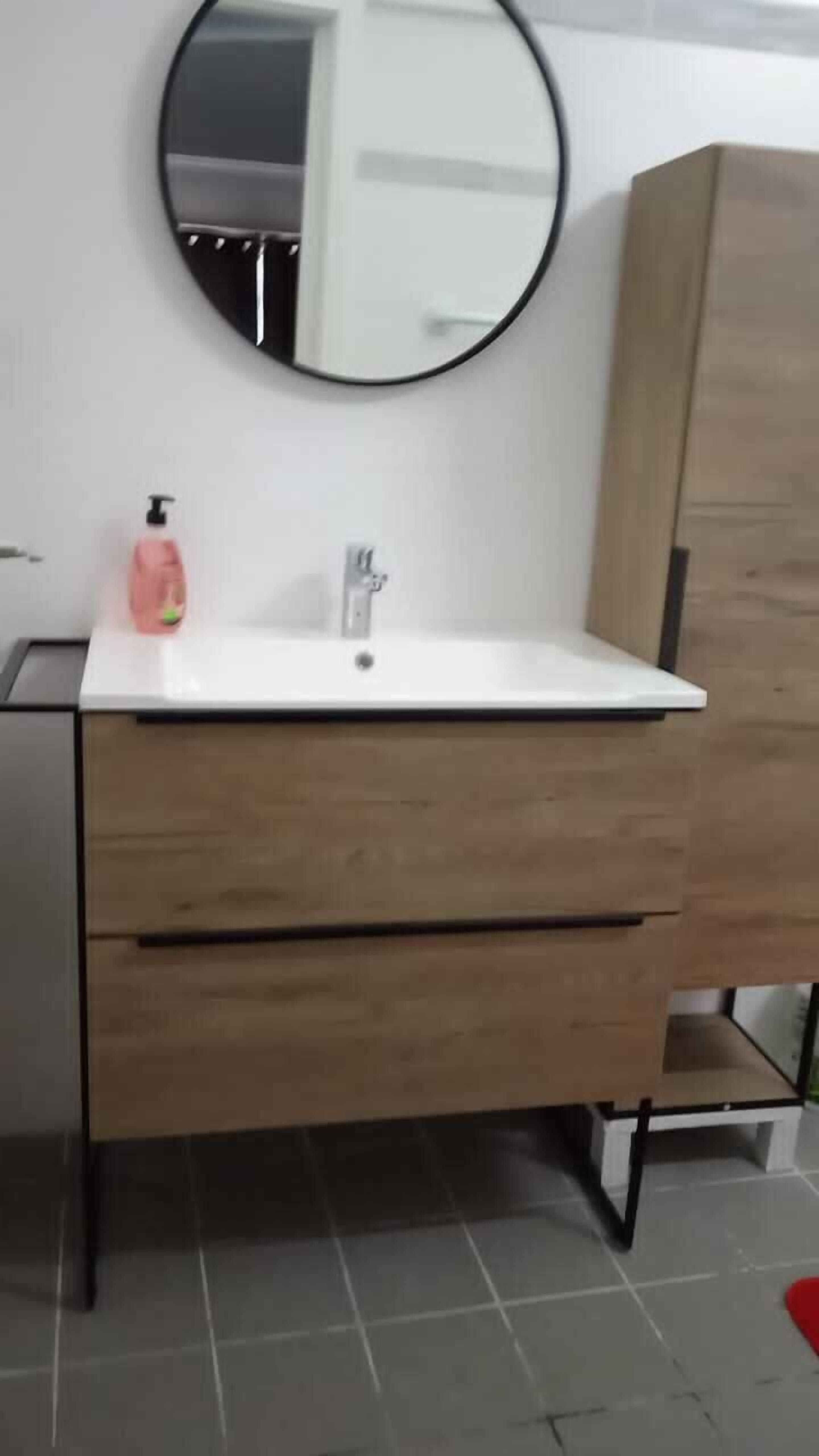 Une salle de bain avec un lavabo blanc, un meuble en bois et un miroir rond.