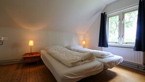A bedroom with a single bed, a nightstand with a lamp, a window with curtains, and a radiator.
