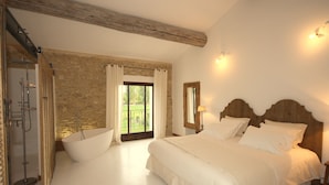 A bedroom with a large bed, a shower, and a view of a garden.