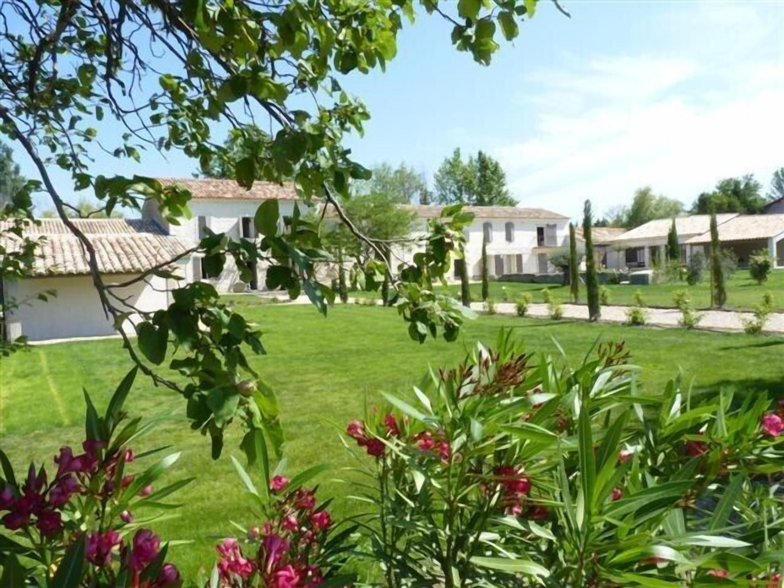 A courtyard with white buildings, green grass, and flowering plants.