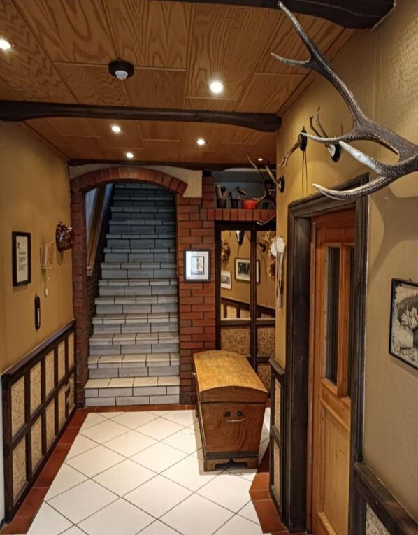 A hallway with a wooden ceiling, a brick staircase, a wooden bench, and a door.