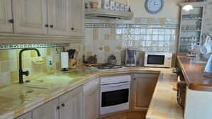 A kitchen with white cabinets, a sink, a stove, an oven, and a clock on the wall. - Village house with lake view (Sainte-Croix-Du-Verdon)