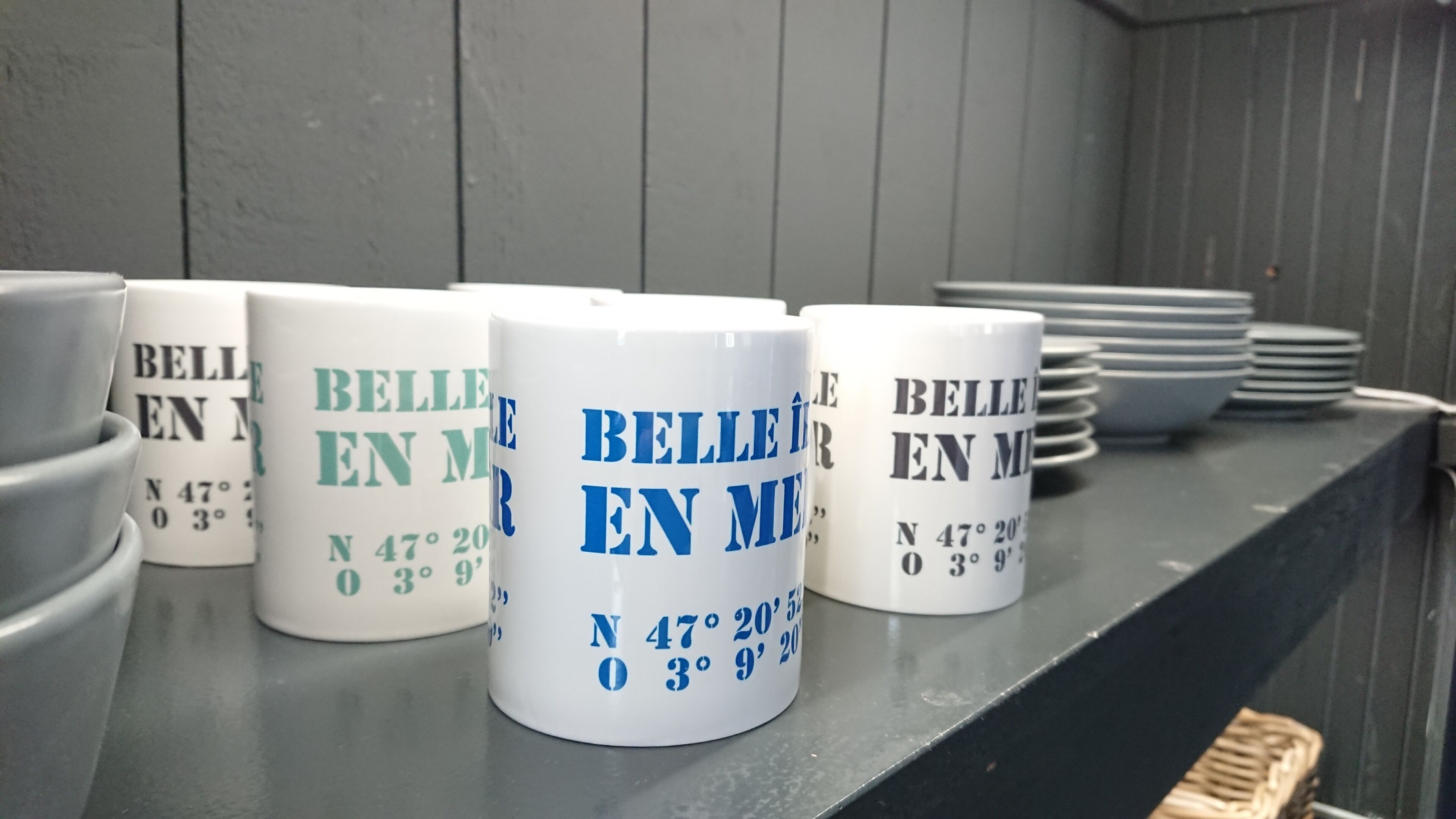 A row of white mugs with text and coordinates on a shelf.