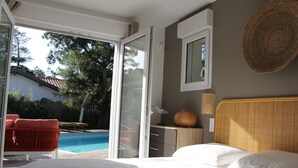 A bedroom with a bed, a view of a swimming pool, and a door leading to an outdoor area with a red chair. - NEW HOUSE, 700M FROM THE BEACH WITH A HEATED SWIMMING POOL AND A SPA (Labenne)