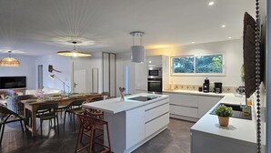 A modern kitchen with a central island, dark tiled flooring, and a dining area with a table and chairs. - NEW HOUSE, 700M FROM THE BEACH WITH A HEATED SWIMMING POOL AND A SPA (Labenne)