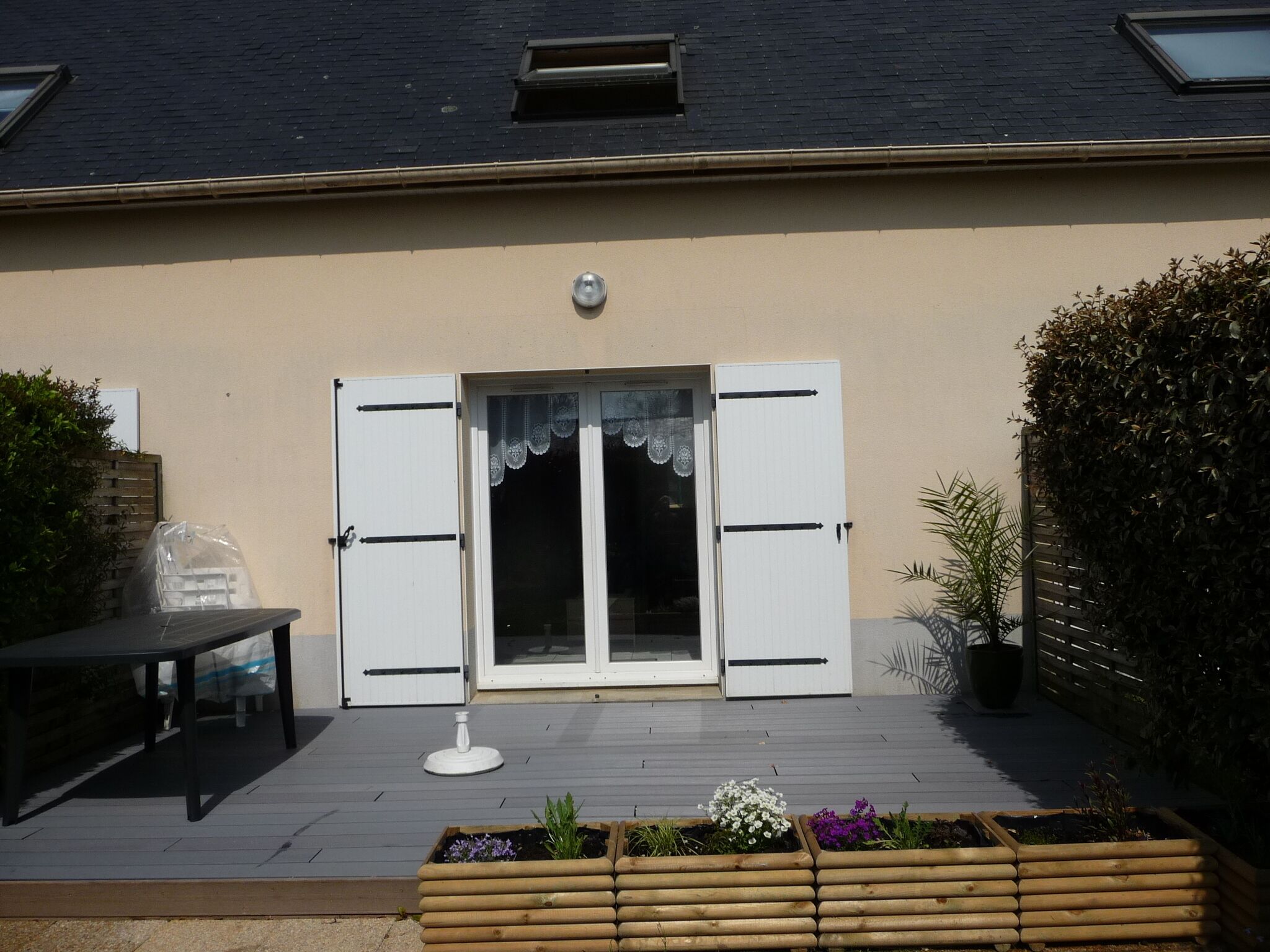 Uma casa com fachada bege, deck de madeira, porta branca com persianas e uma pequena janela acima da porta.