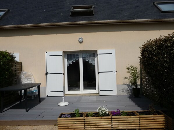 A house with a beige exterior, a wooden deck, a white door with shutters, and a small window above the door.