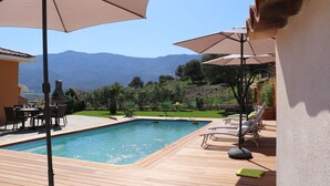 Ein Schwimmbad mit Holzterrasse, Gartenmöbeln und Sonnenschirmen.