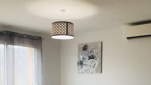 Ein modernes Wohnzimmer mit einer Eckcouch, einem kleinen Hocker, einer Pendelleuchte und einer Wand-Klimaanlage.