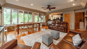 A spacious living room with a brown leather sofa, ottomans, and a dining area with wooden chairs and a table. - Spacious Lake Home w/ Dock, Hot Tub & Views (McHenry)
