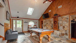 A pool table in a room with stone walls, a wooden ceiling, and a gray sofa. - Spacious Lake Home w/ Dock, Hot Tub & Views (McHenry)