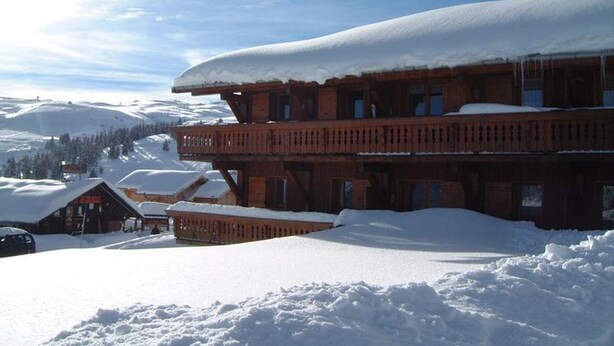 Una cabaña de madera con varios balcones, rodeada de montañas nevadas y un cielo despejado.